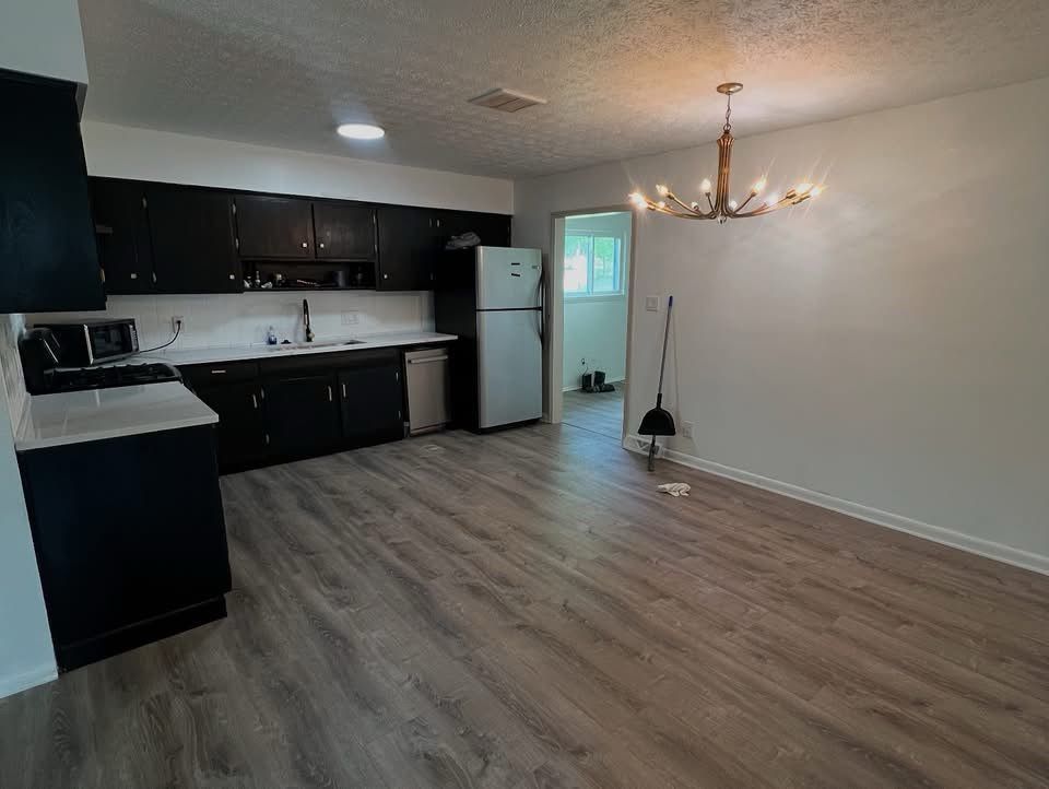 Empty kitchen and dining area with dark cabinets, white appliances, and wood-look flooring