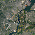 Aerial view of a city divided by a winding river, with bridges and dense urban buildings on both sides.