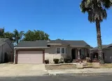Single-story suburban house with pink garage door, front porch, and tall palm tree under a blue sky