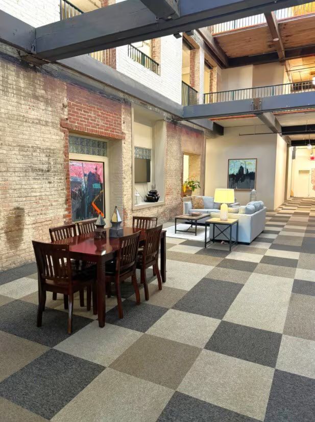 Interior with checkered floor, dining table, sofa, exposed brick walls, and metal beams.