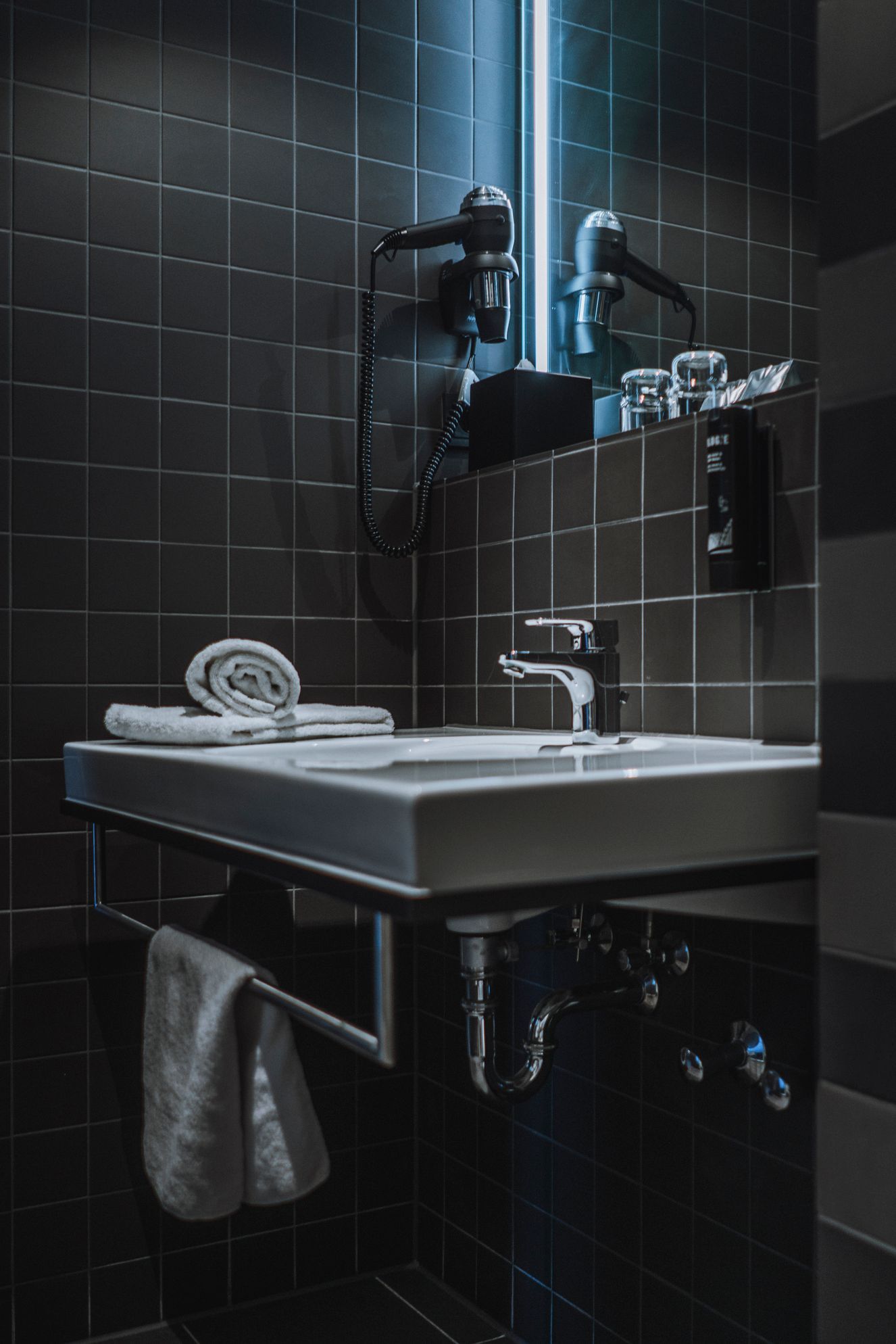 Modernes, schwarz gefliestes Badezimmer mit wandmontiertem Waschbecken, Spiegelschrank und Handtuchablage
