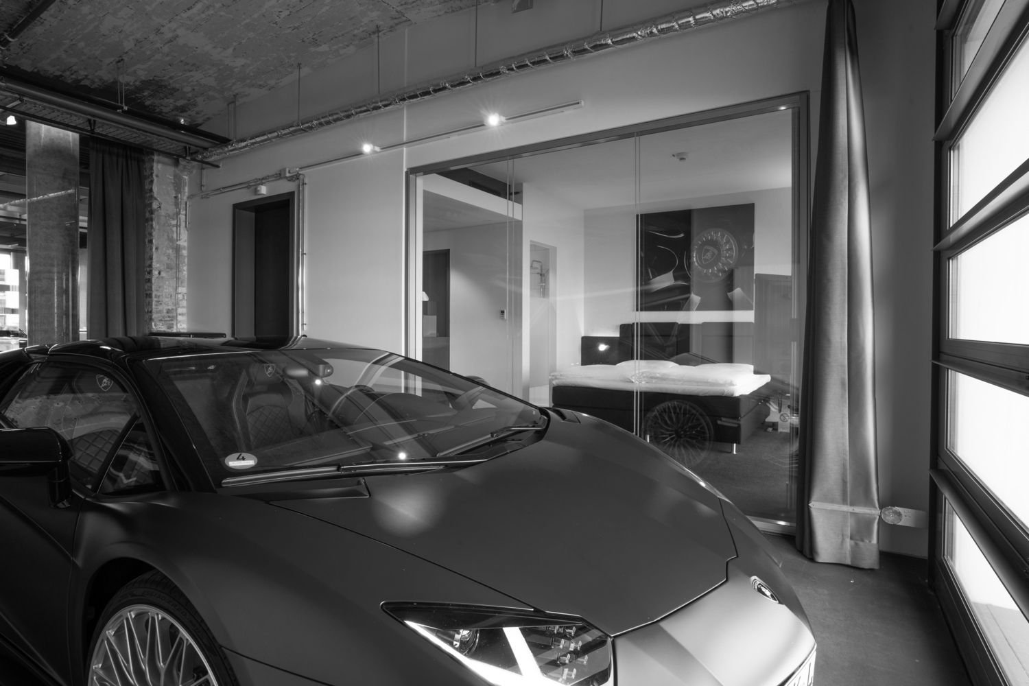Ein schwarzer Sportwagen steht in einer modernen Garage mit Glaswänden und dahinter befindet sich ein heller Wohnbereich.