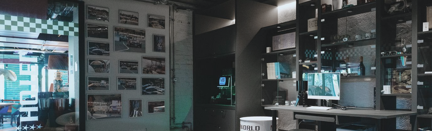 Das Interieur eines Elektronikgeschäfts wirkt etwas düster, mit Wanddisplays, Monitoren und einem Tresen, der von türkisfarbenen Bildschirmen beleuchtet wird.