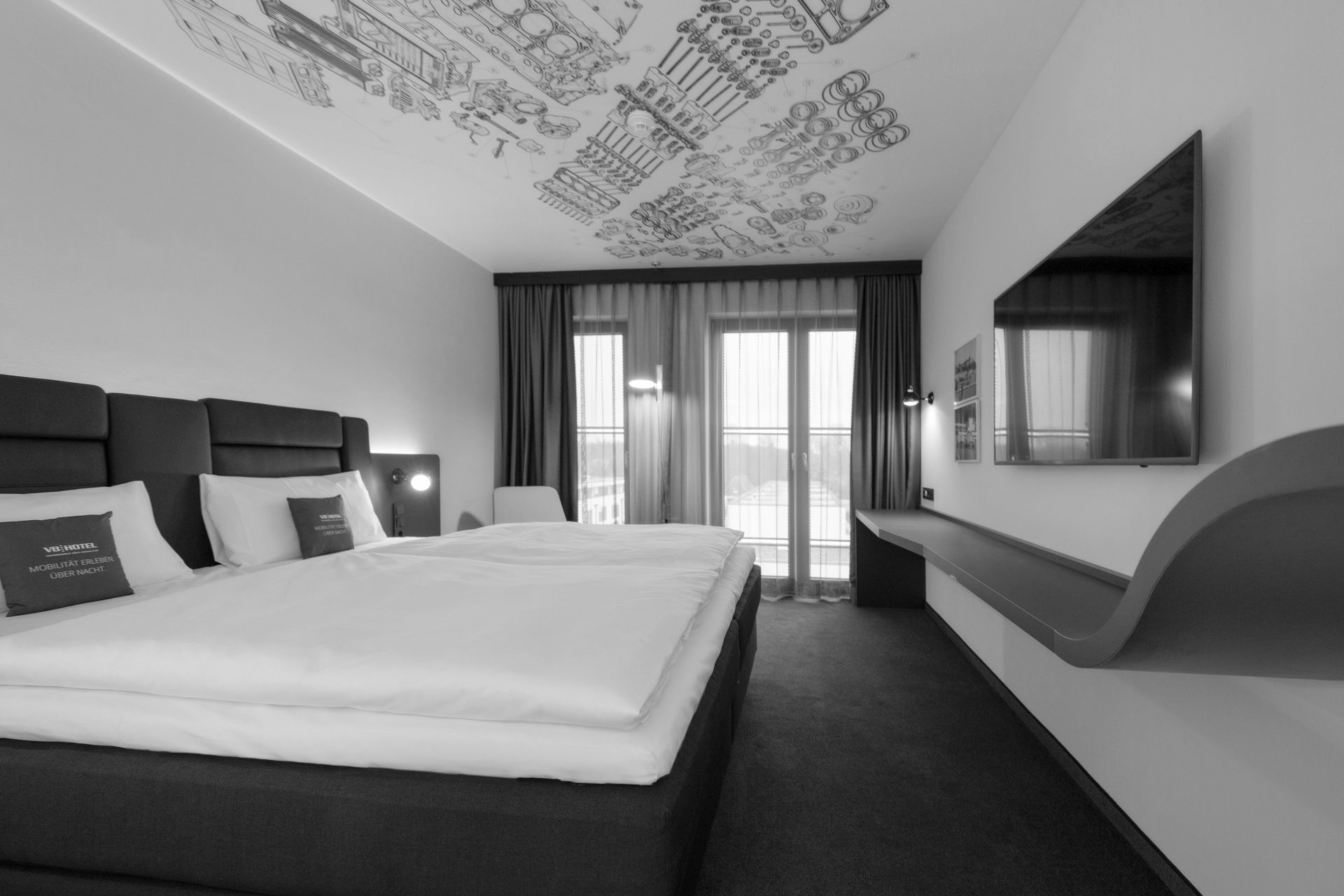 Modernes Hotelzimmer mit großem Bett, Wandfernseher, Schreibtisch und Balkontüren