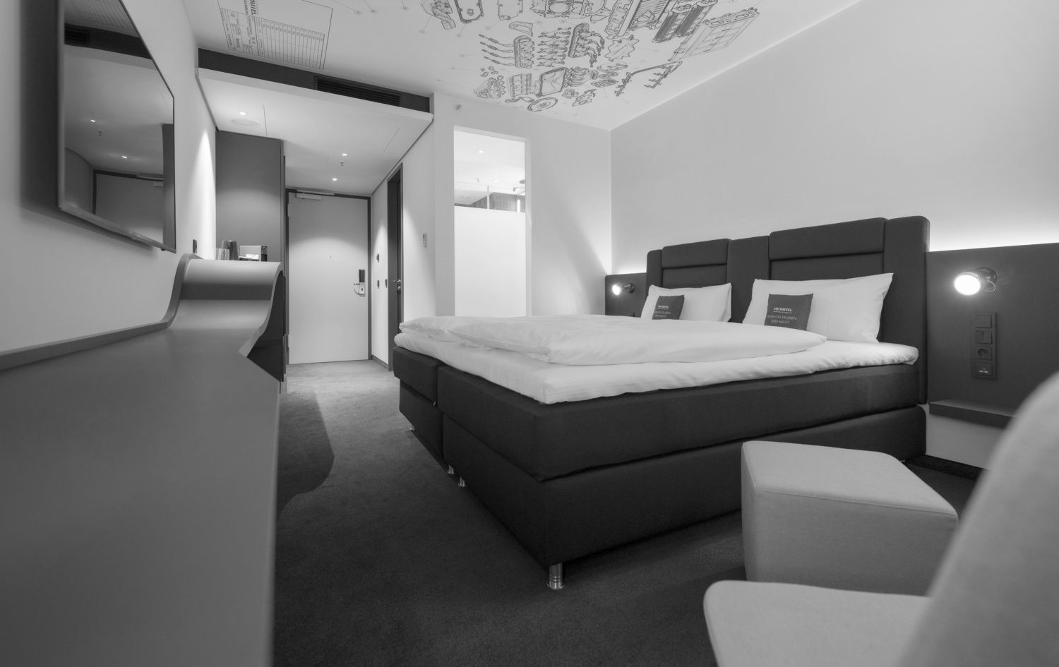 Modernes Hotelzimmer mit Kingsize-Bett, grauem Teppichboden und hellem schwarz-weißem Deckengemälde.