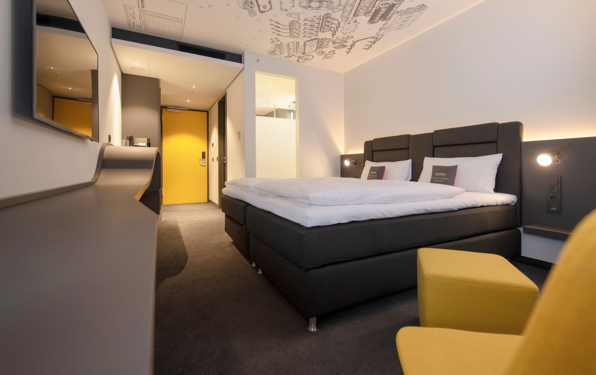 Modernes Hotelzimmer mit großem Bett, gelbem Sessel und warmem Licht