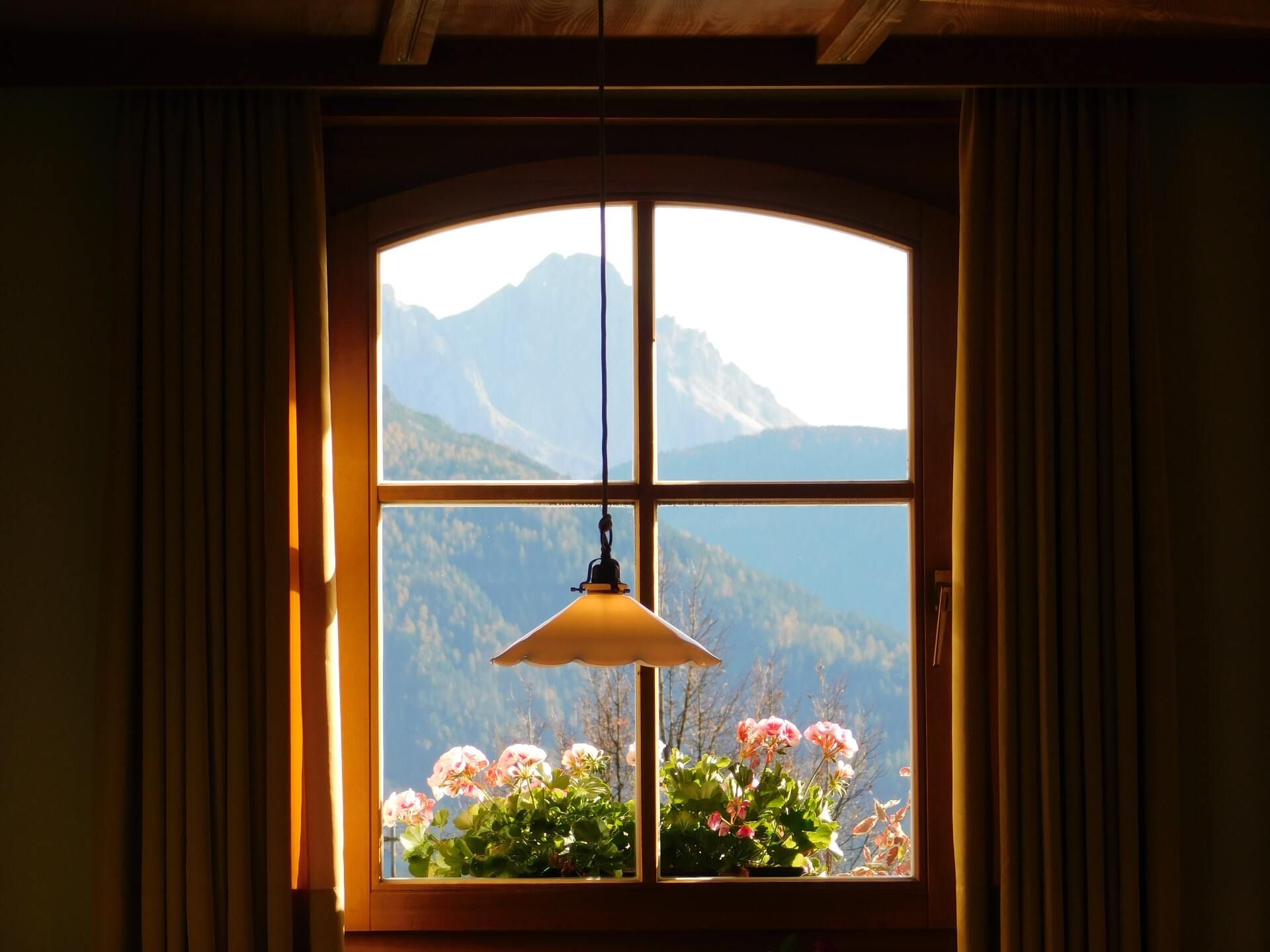 Sonnendurchflutetes Fenster mit Bergblick, Hängelampe und Blumen auf der Fensterbank
