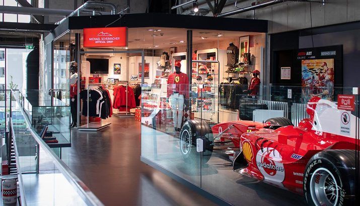 Ein roter Formel-1-Rennwagen ist in einem Motorsportmuseum zusammen mit Rennbekleidung und Erinnerungsstücken ausgestellt.