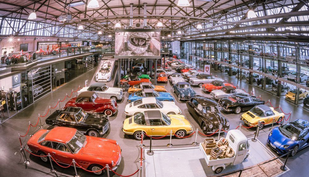 Klassische Automobile werden in einem großen, überdachten Automobilmuseum unter hellen Oberlichtern ausgestellt.