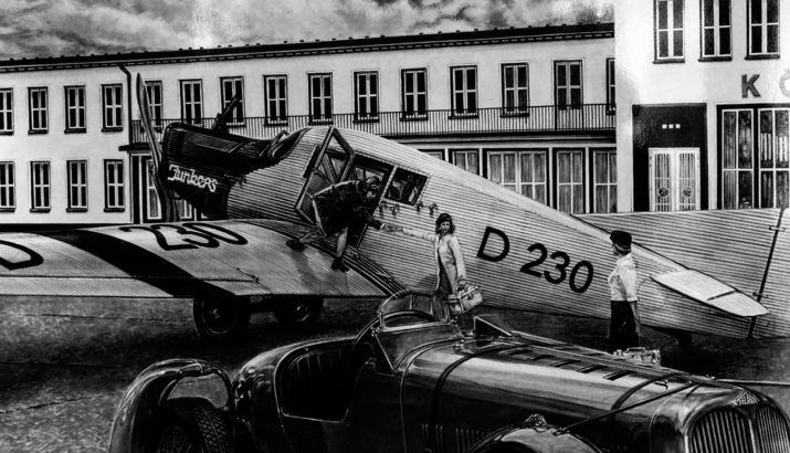 Schwarz-Weiß-Aufnahme einer Unfallstelle mit einem beschädigten Flugzeug mit der Kennung D 230 und einer Person, die daneben auf einer Landebahn steht.