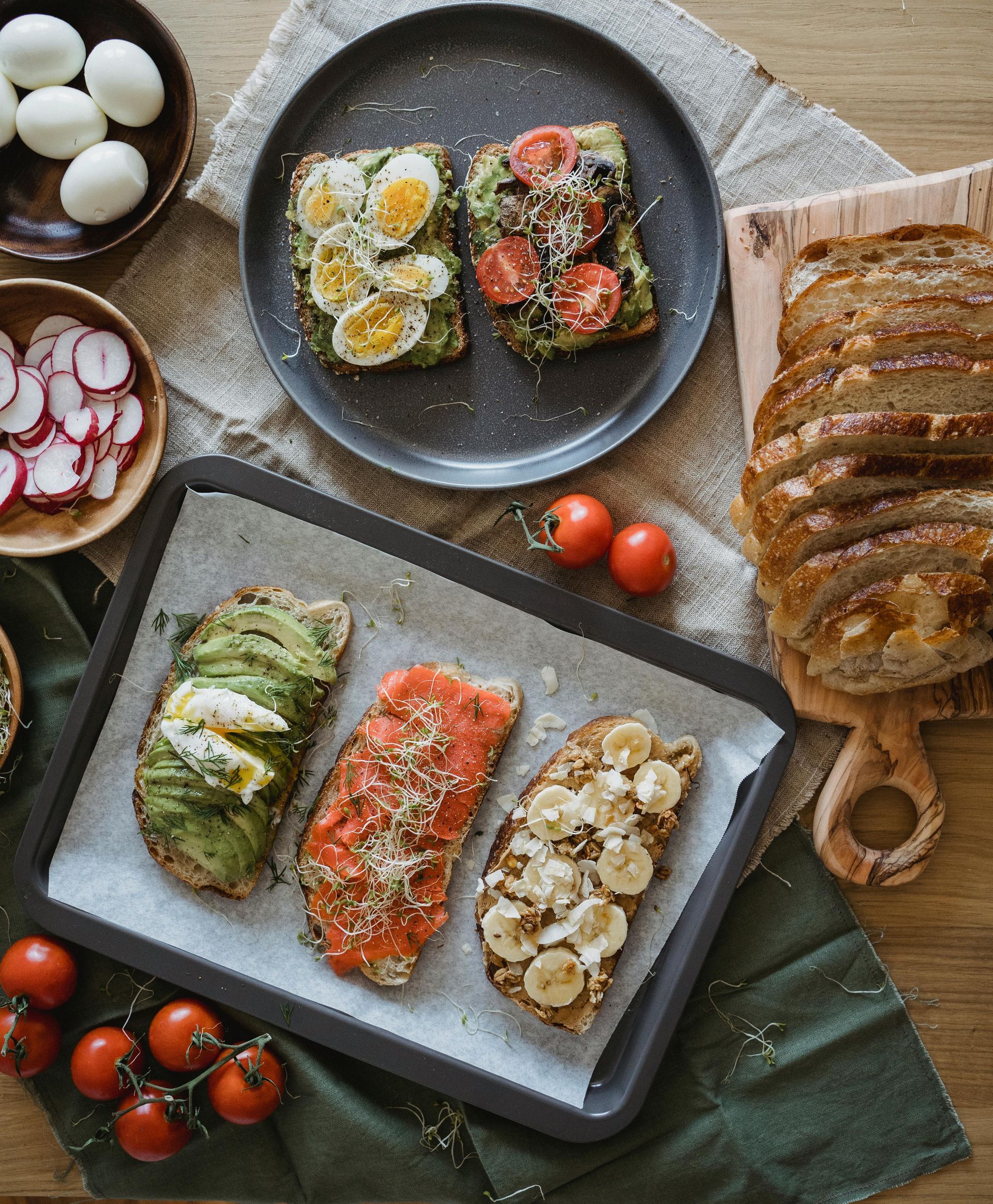 Verschiedene offene Sandwiches auf dunklen Tellern mit Eiern, Avocado, Lachs, Pilzen, Tomaten und Brot.
