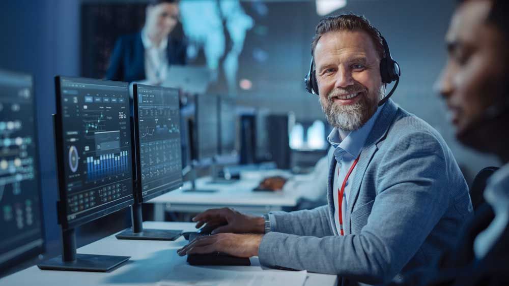 A man wearing a headset is sitting at a desk in front of a computer.