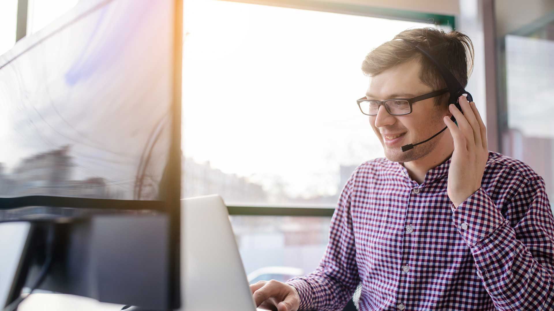 A man wearing a headset is sitting in front of a laptop computer.