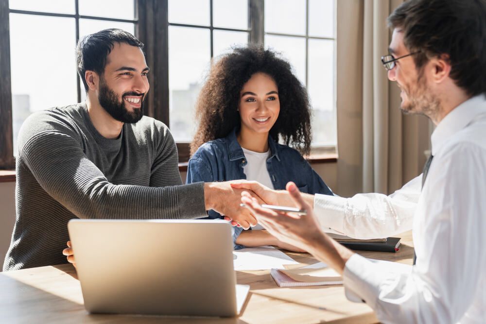 A man and woman are shaking hands with a man while sitting at a table with a laptop.