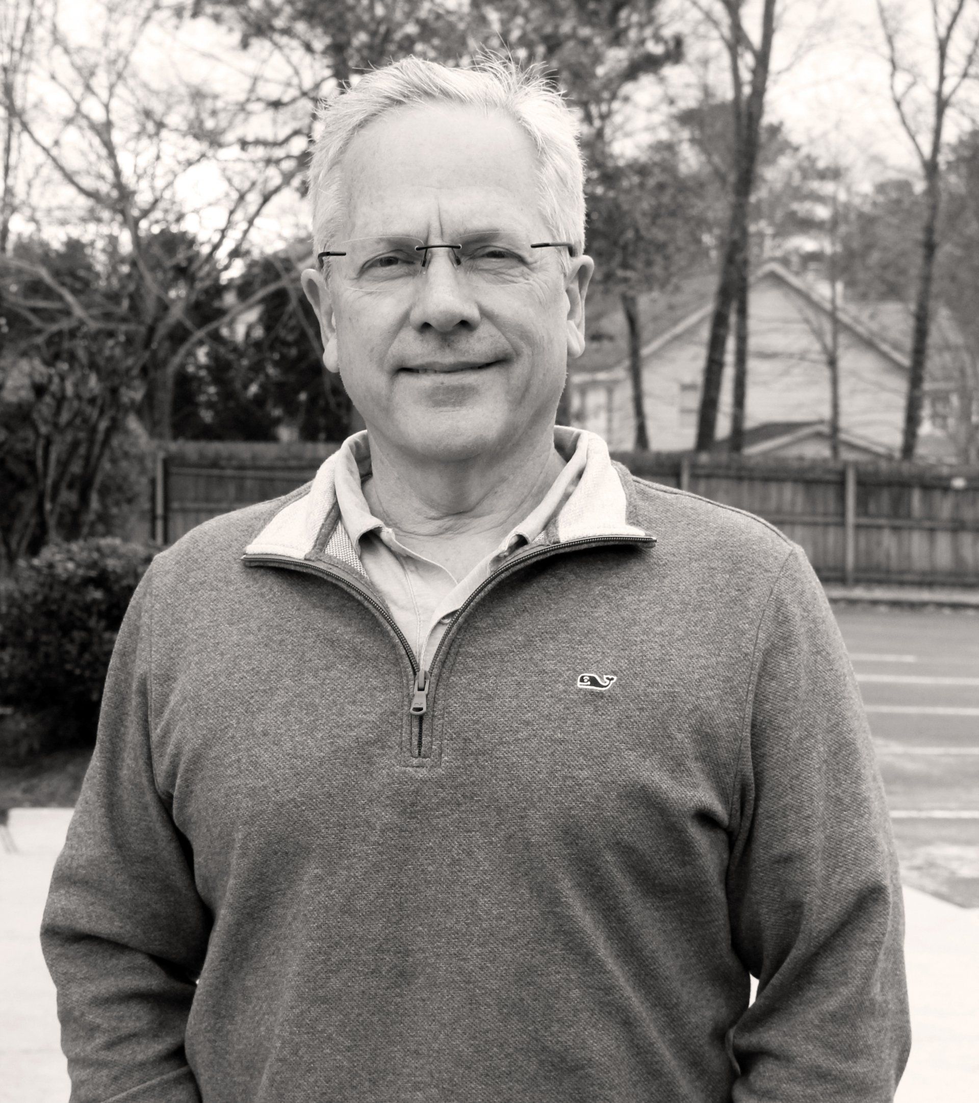 Man in glasses and sweater, smiling outdoors in front of trees and a house. Bill Boldt
