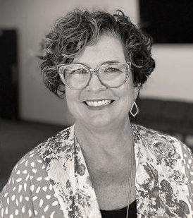 Woman with glasses smiles, wearing floral top and earrings. Kari Glemaker