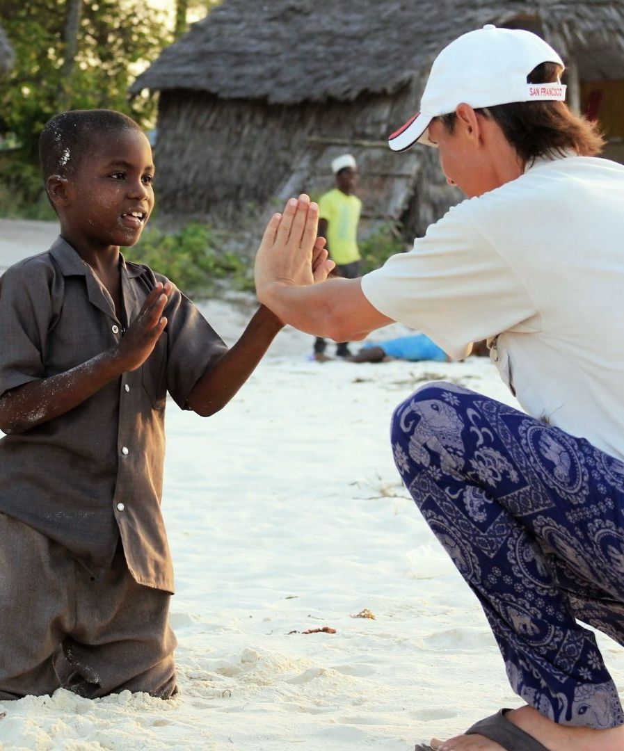 Child and person playing patty-cake on a sandy beach.
