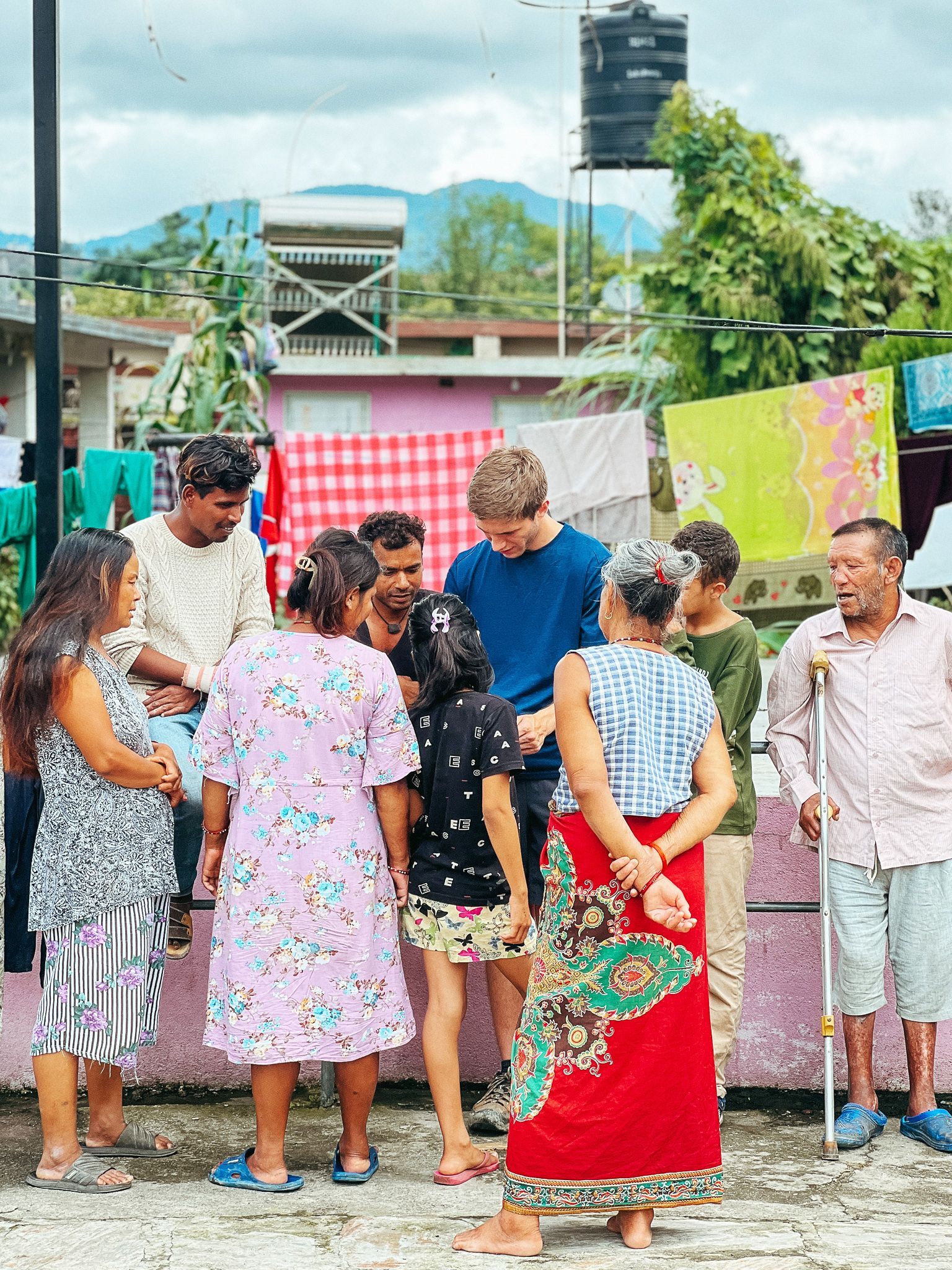 Group of people on a rooftop, possibly interacting with each other. Clotheslines and city views in background.