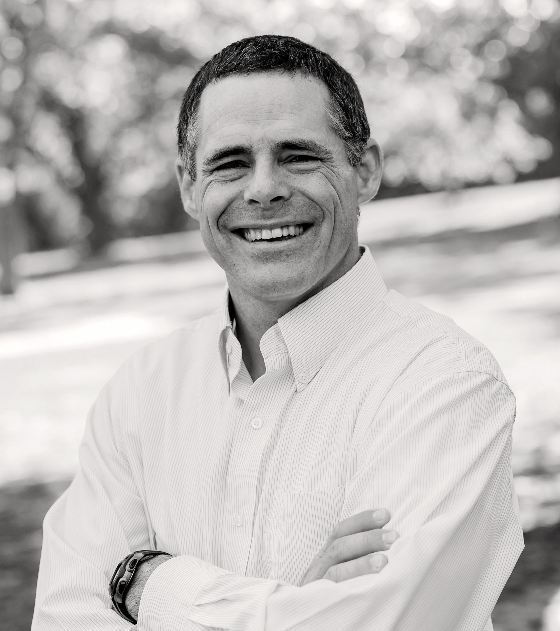 Man with arms crossed smiling, outdoors, wearing a collared shirt. Hoffman Rhyne