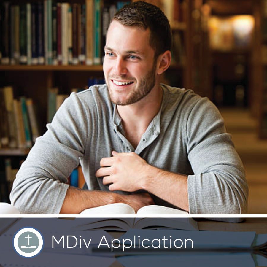 Man smiles while studying in a library. Open book, bookshelves in background. MDiv application graphic.