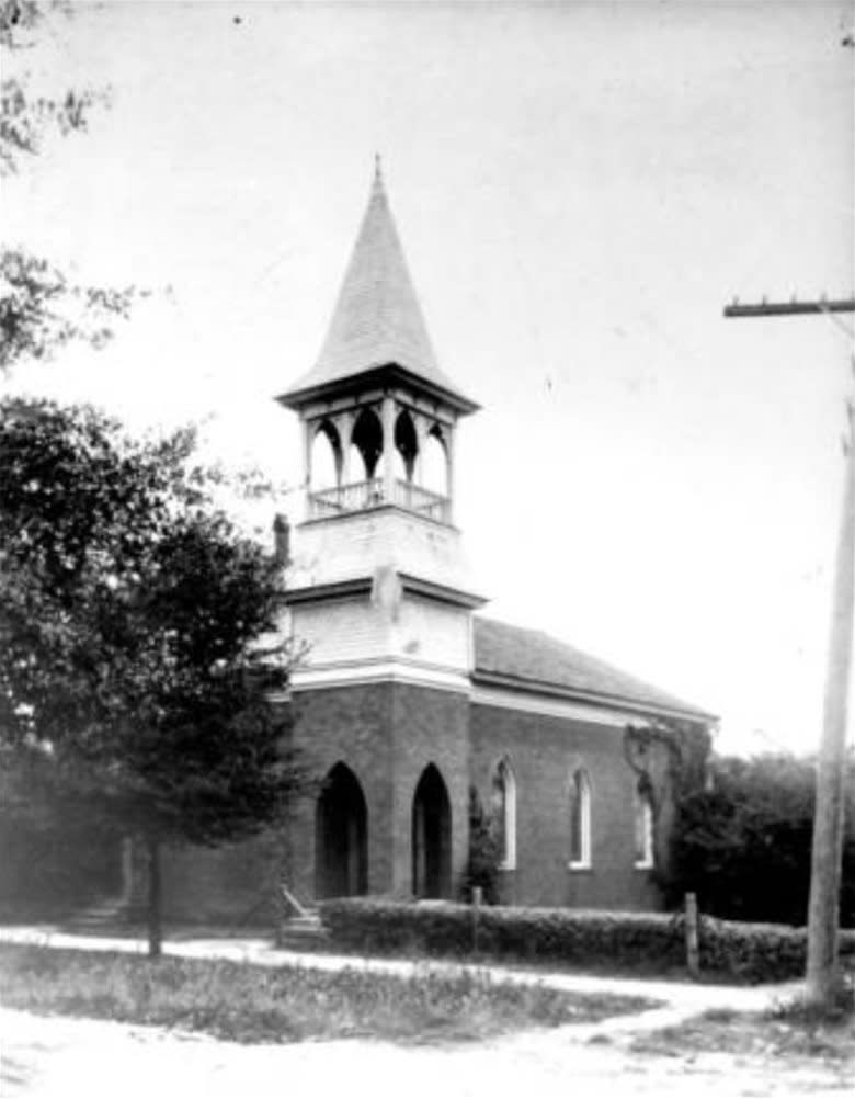 Brick church with steeple, arched windows, and a surrounding hedge. Auburn University Chapel.