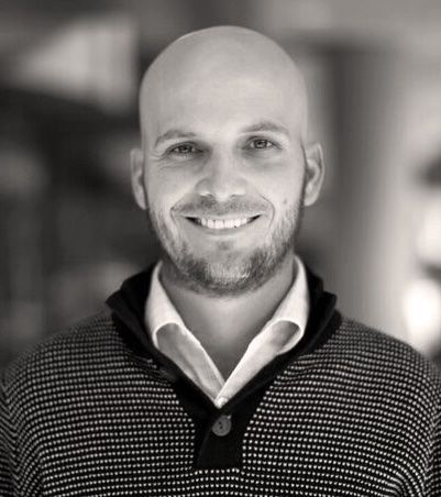 Bald man smiles, wearing a patterned sweater over a white collared shirt. Bo Smith