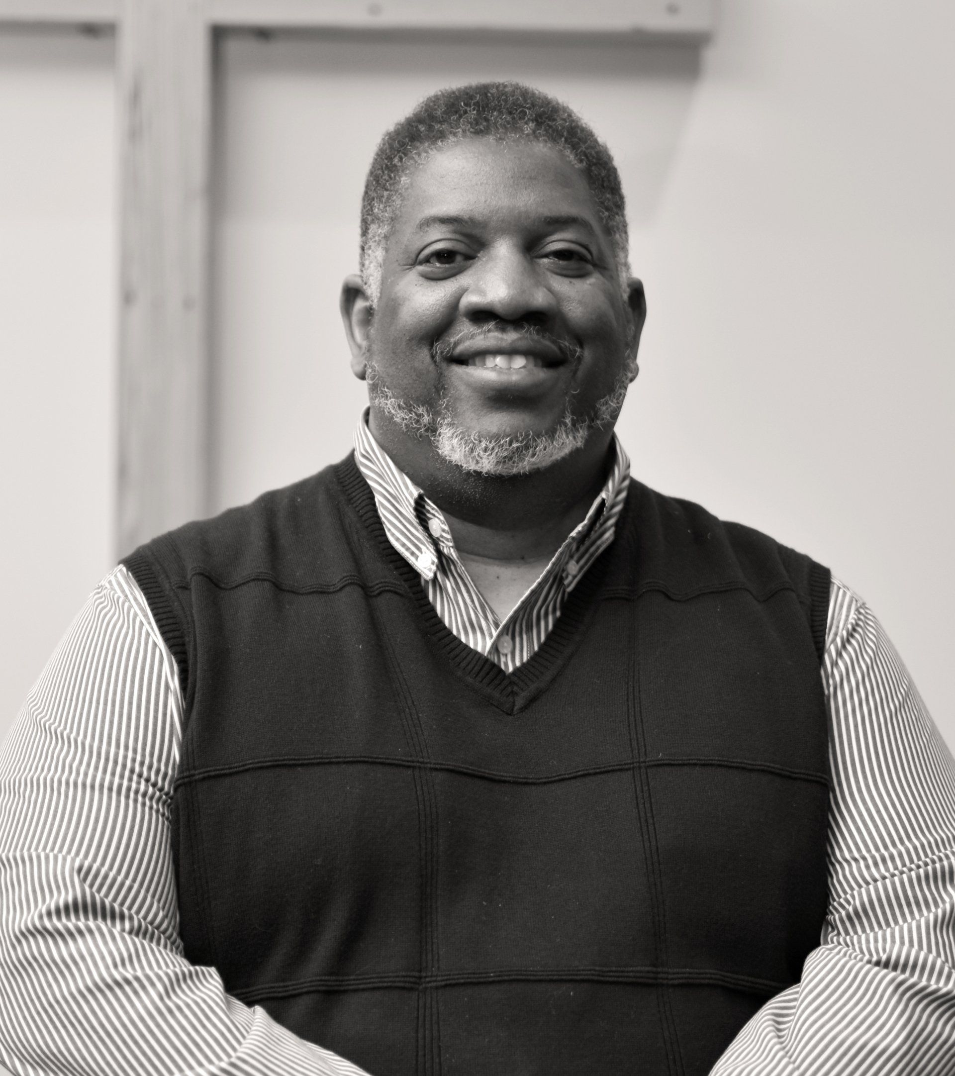 Man smiling in front of a light background. Wearing a vest over a collared shirt. JArthur Grubbs