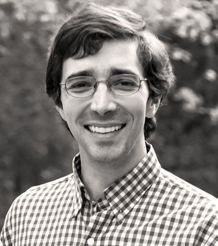 Man wearing glasses and a checkered shirt smiles outdoors. Jere Scott Bradshaw