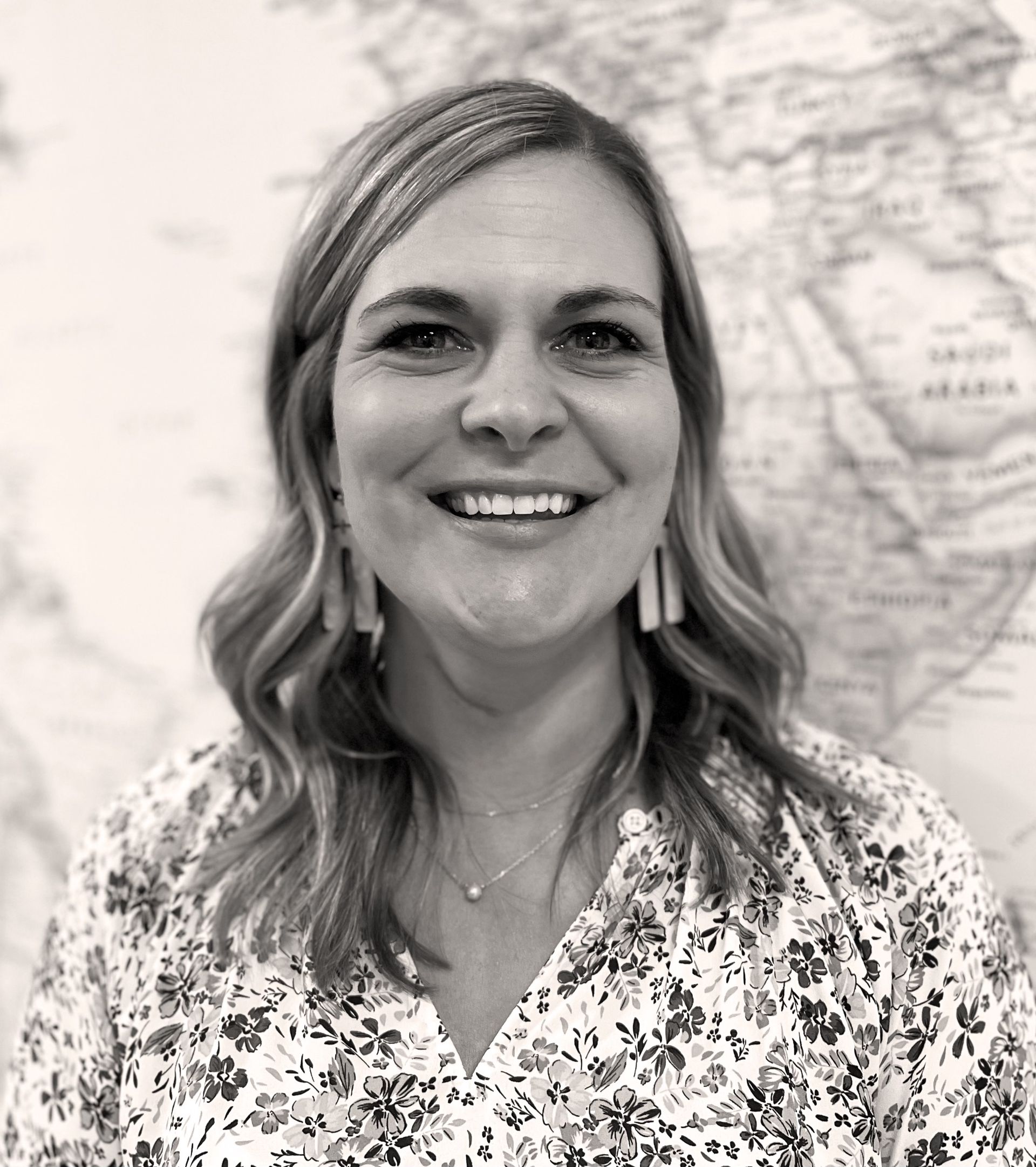 Woman smiling, floral print shirt, against a world map backdrop.