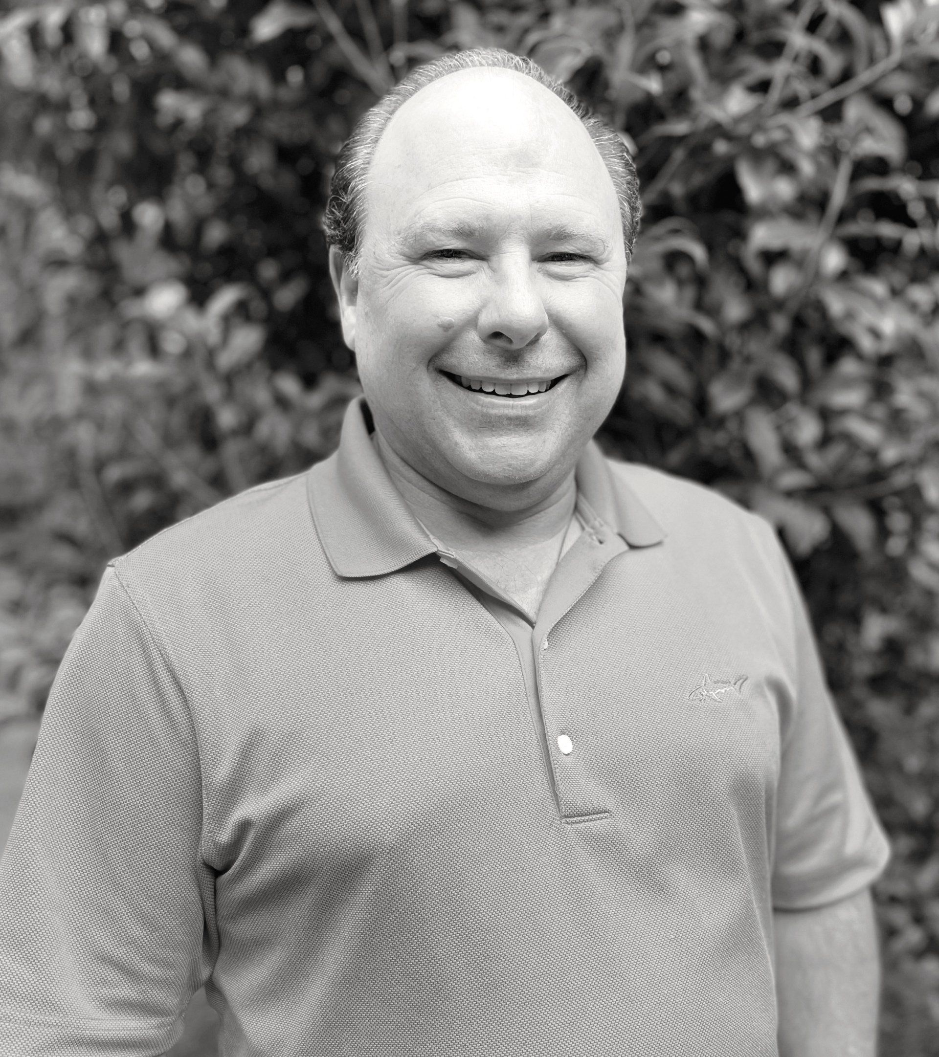 Smiling man wearing a polo shirt, standing in front of leafy foliage. Tim Kurtaneck