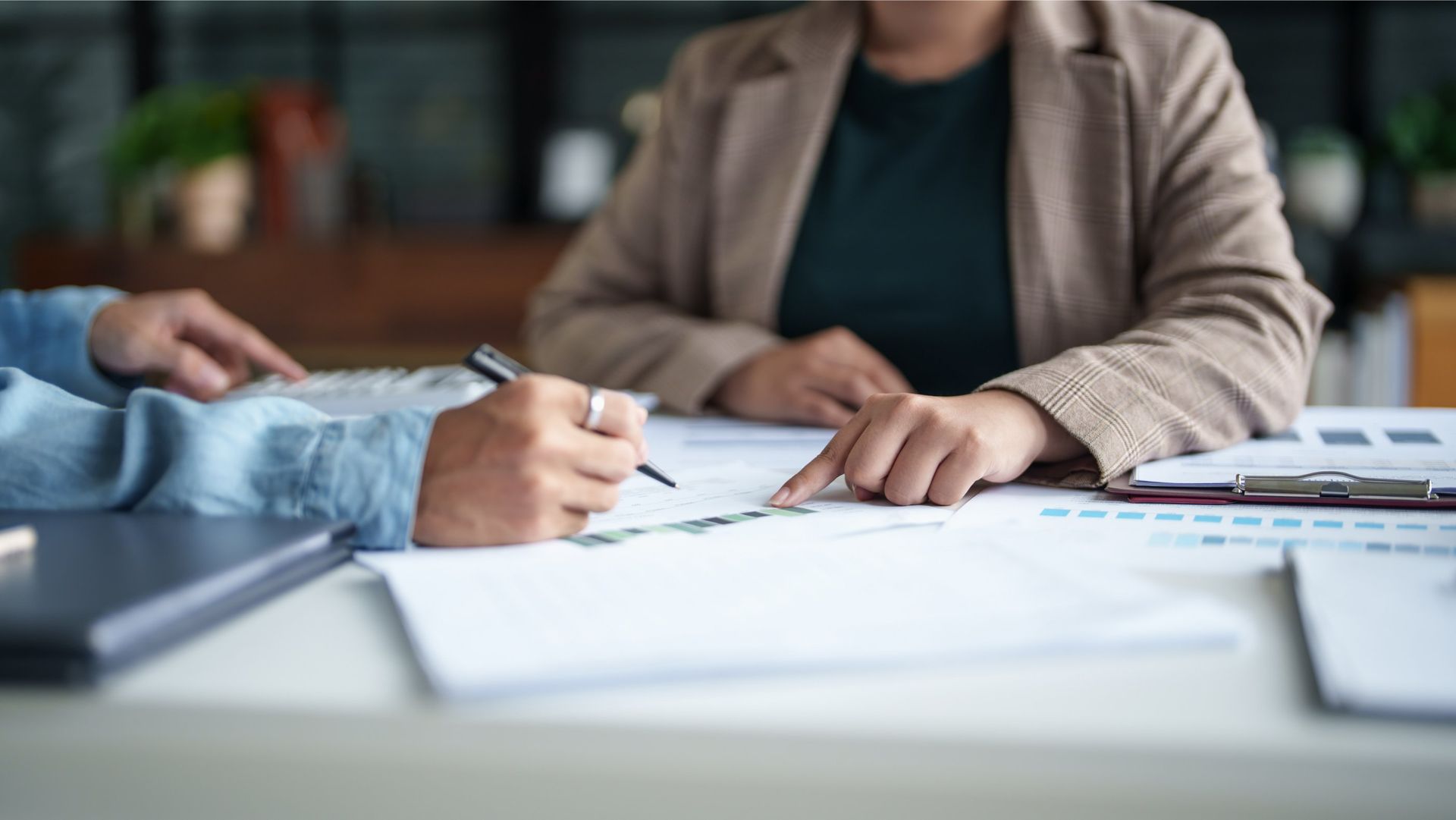 Two people reviewing documents, one signing, in an office setting.