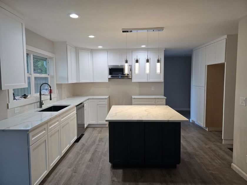 Modern white kitchen with a dark island, stainless appliances, and pendant lights
