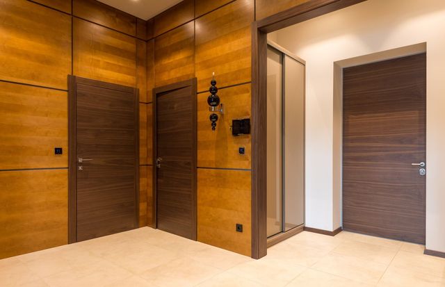 Modern hallway with wood-paneled walls, beige floor, and two closed doors.