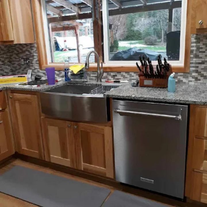 Kitchen sink and stainless dishwasher beneath a window, with wooden cabinets and knife block on the counter