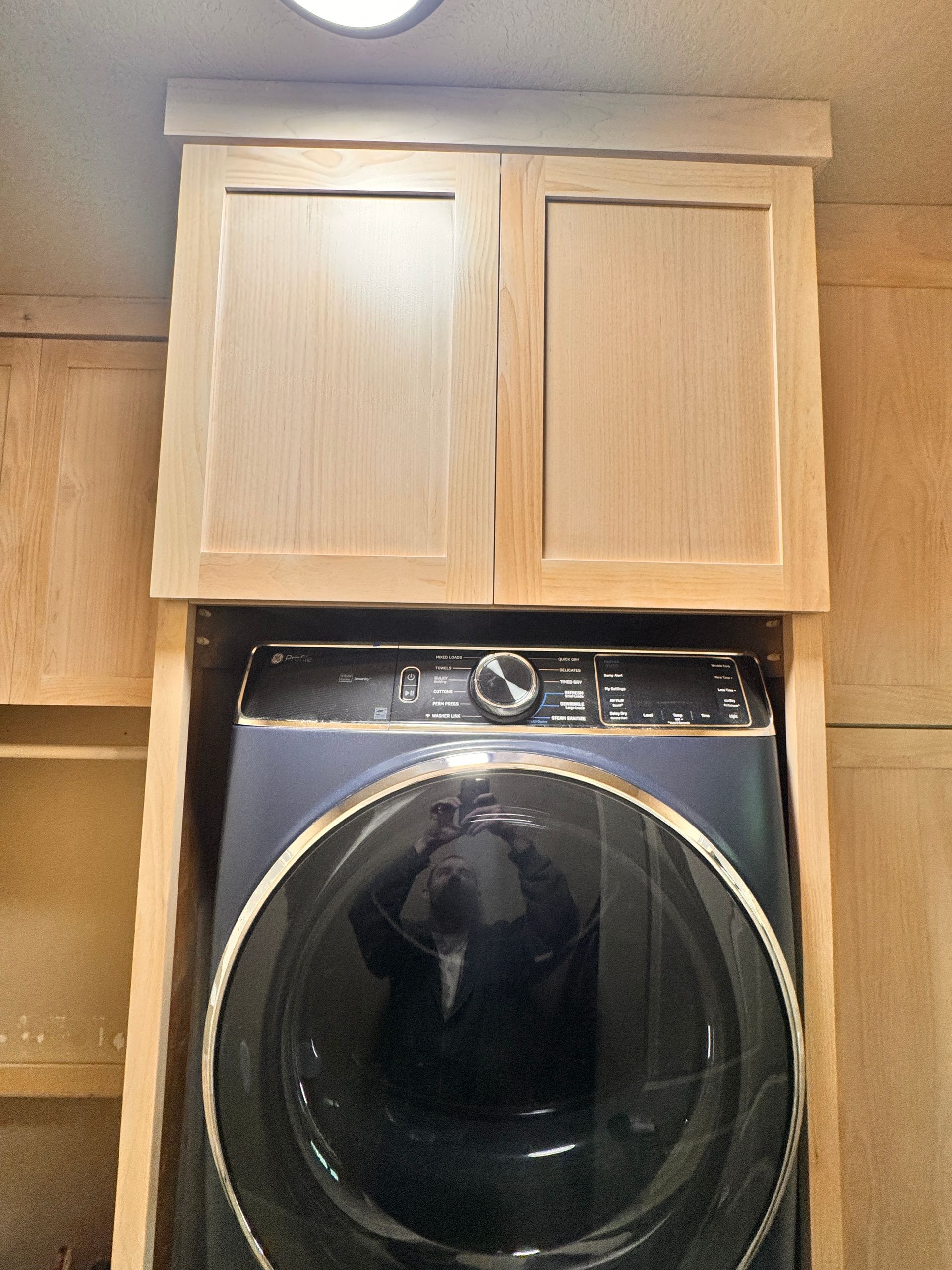 Laundry area with stacked wooden cabinets above a front-loading washing machine.
