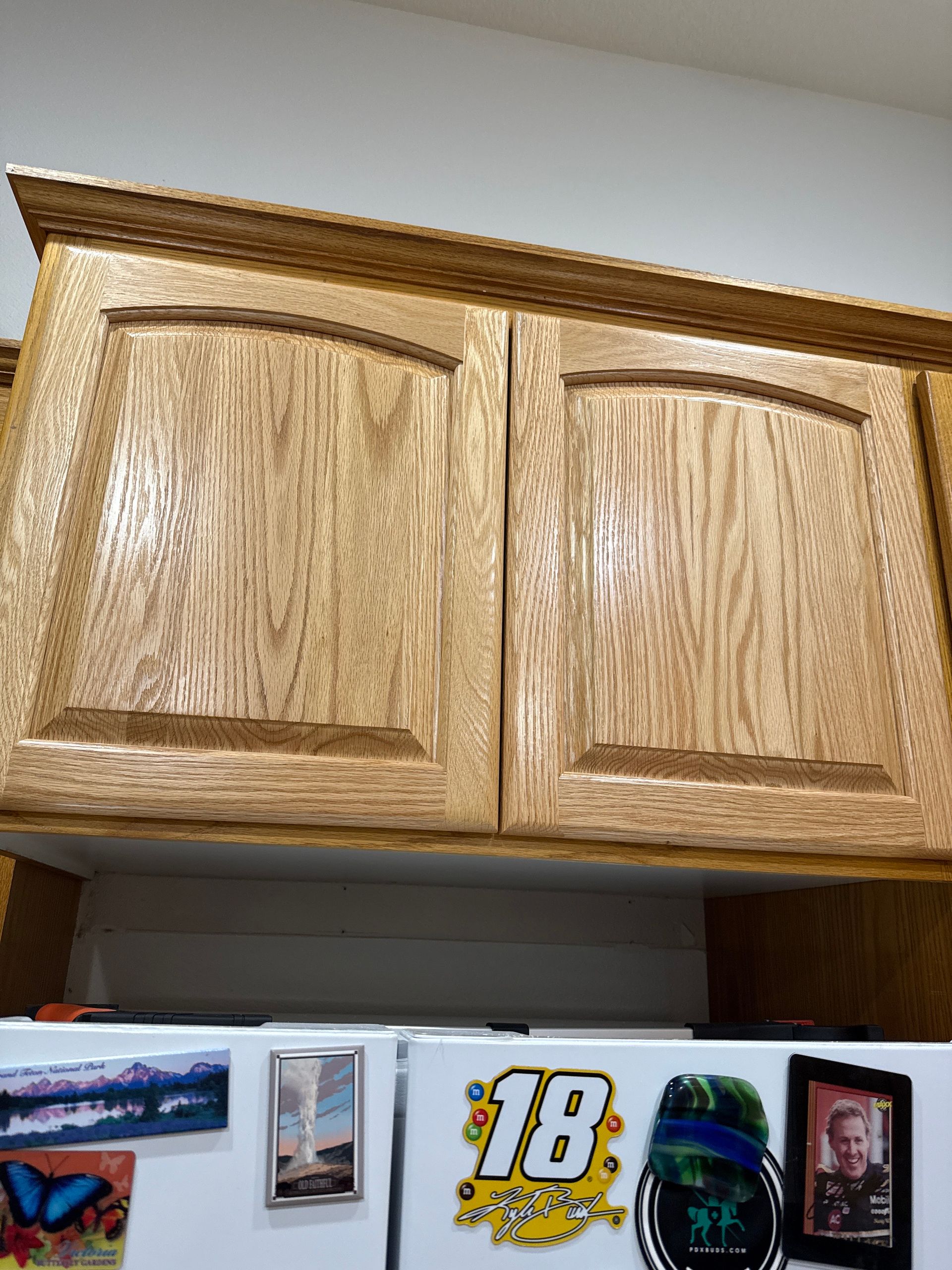 Wooden kitchen cabinet above a refrigerator with photos and sports magnets on the door