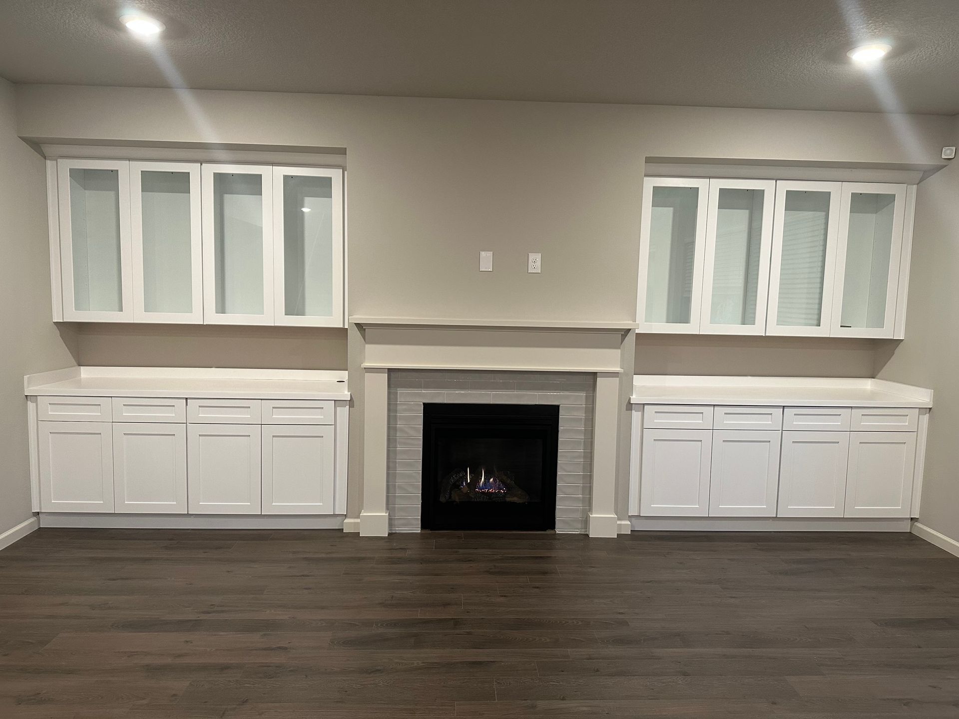 Built-in cabinets and windows flanking a central fireplace in a beige room with dark wood flooring