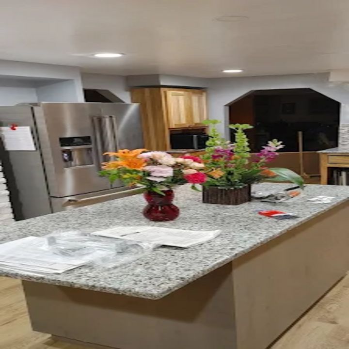 Kitchen island with a flower centerpiece, granite countertop, and stainless steel refrigerator in the background