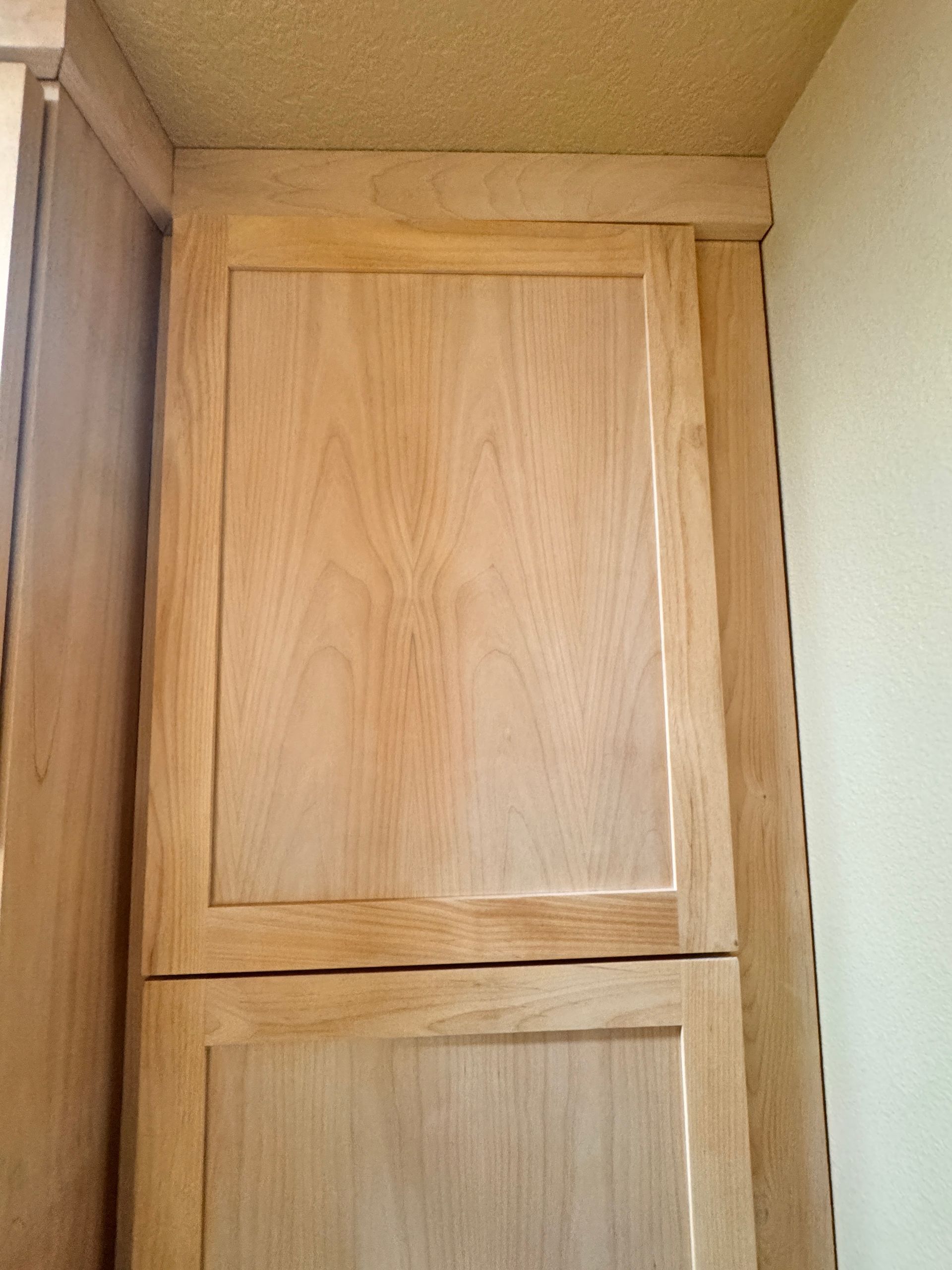 Tall wooden cabinet with two paneled doors in a corner under a ceiling.