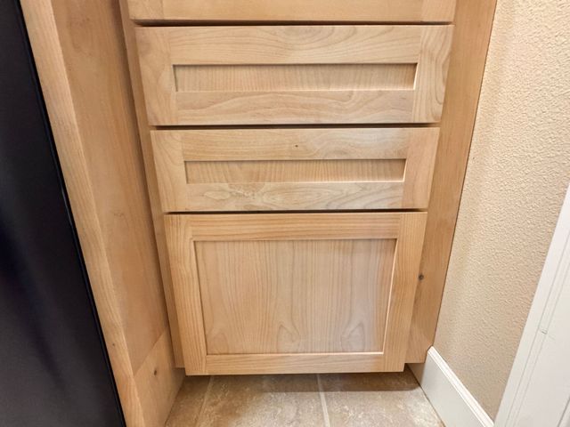 Wooden bathroom vanity cabinet with three drawers and a lower door beside a beige wall.