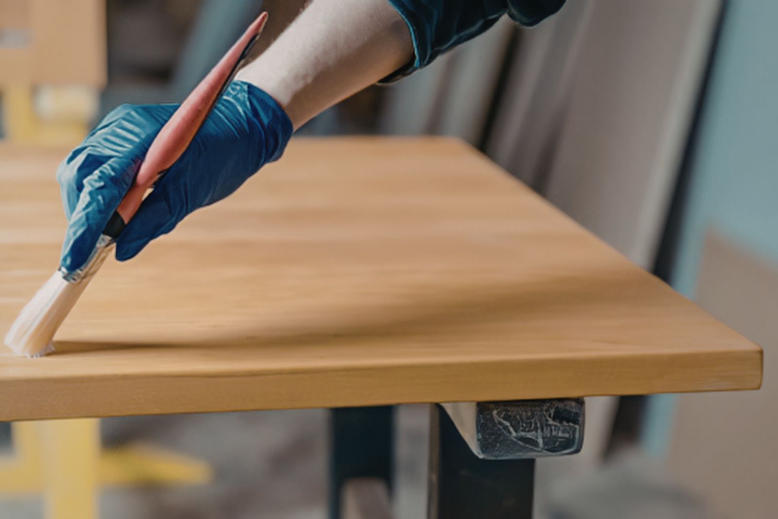 Gloved hand applying finish to a wooden tabletop with a brush