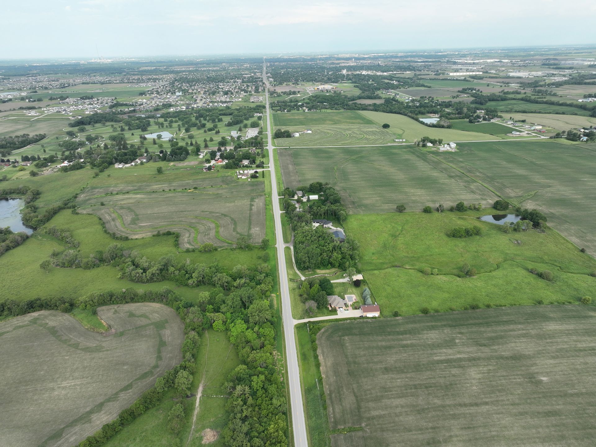 An aerial view of a road going through a lush green field