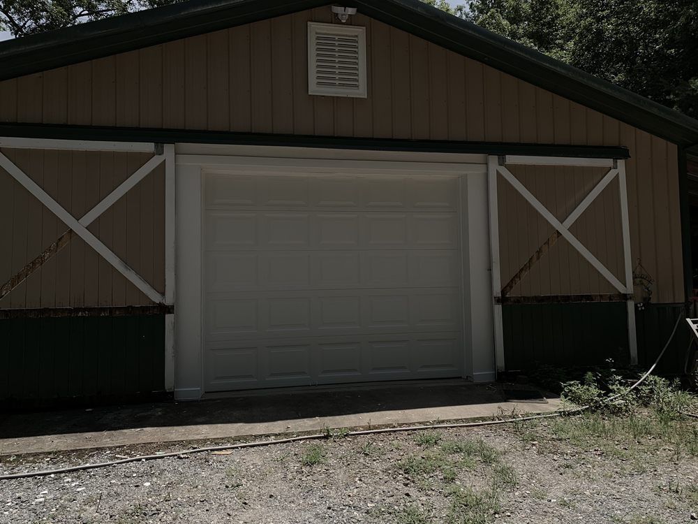 White garage door on a tan barn-style building with green trim and white X-braced side panels.