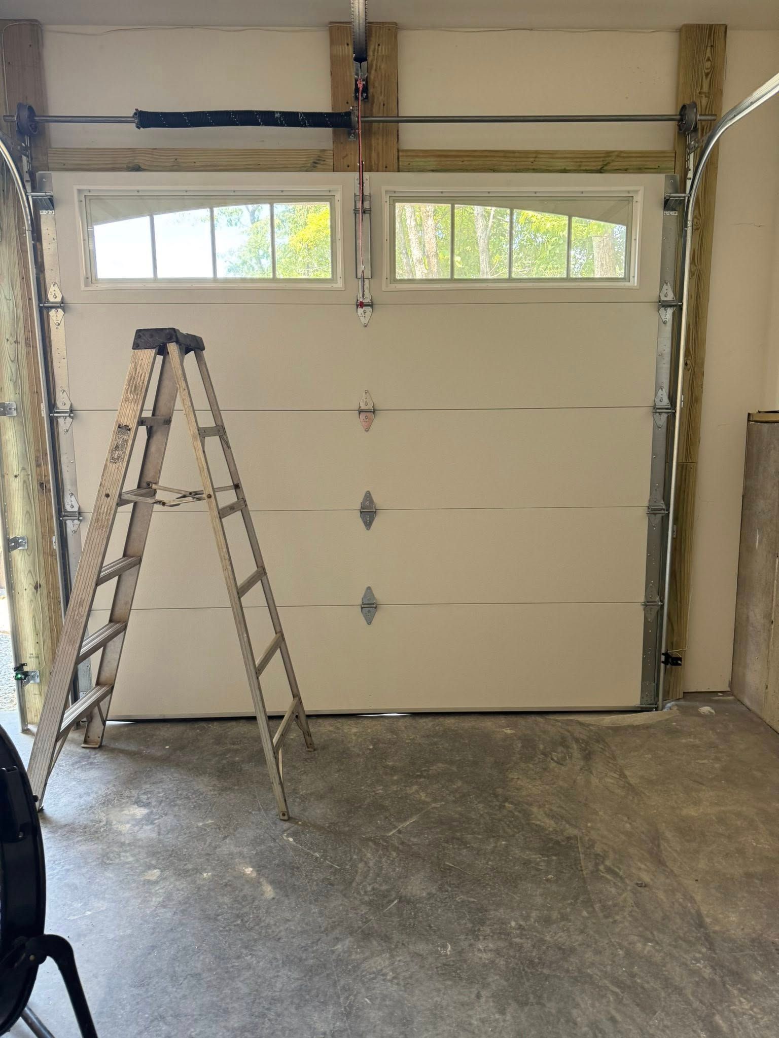 A garage door with four windows, a step ladder, and unfinished concrete floor and walls.