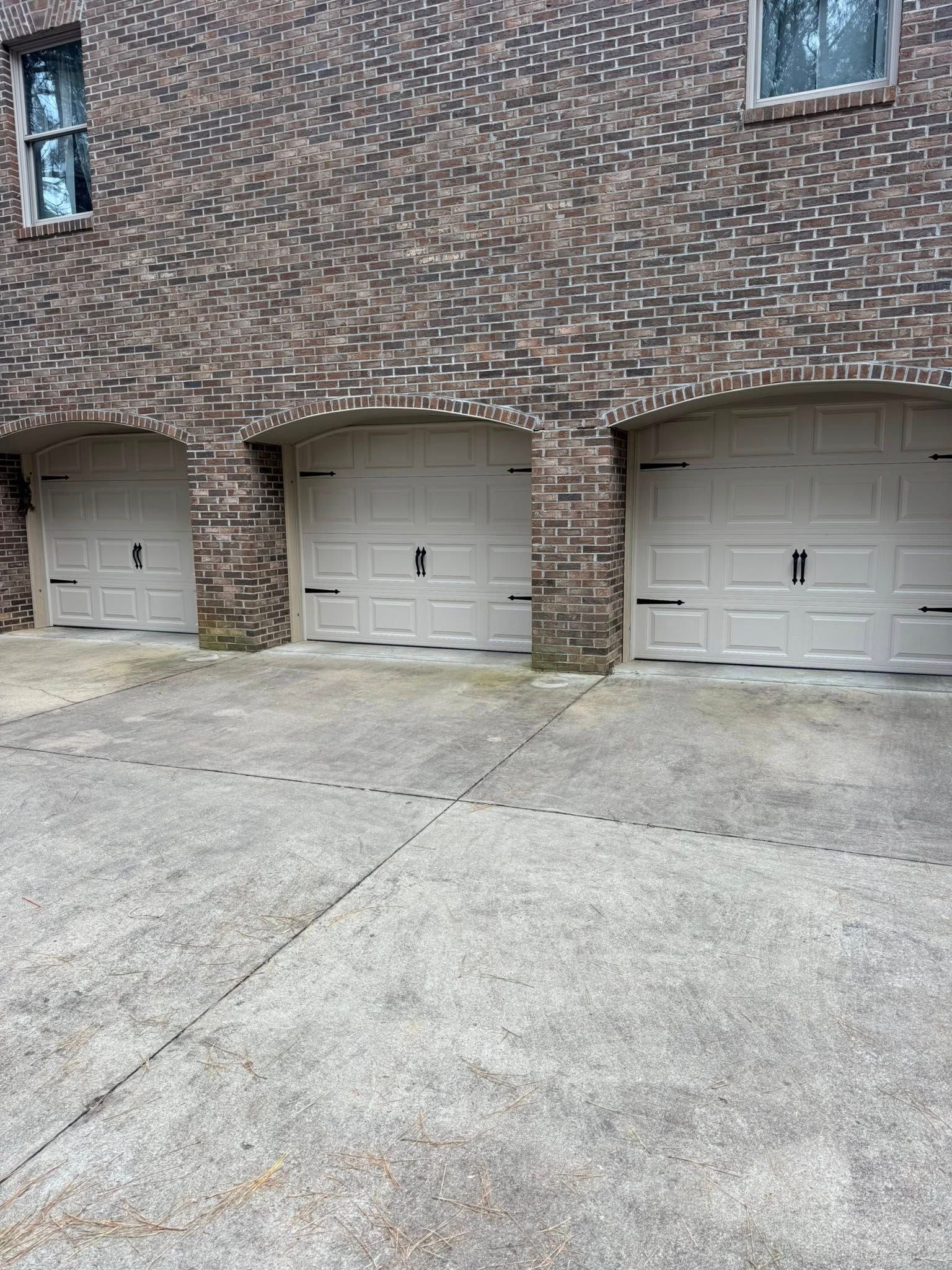 Three beige garage doors beneath a brick exterior with a concrete driveway in front