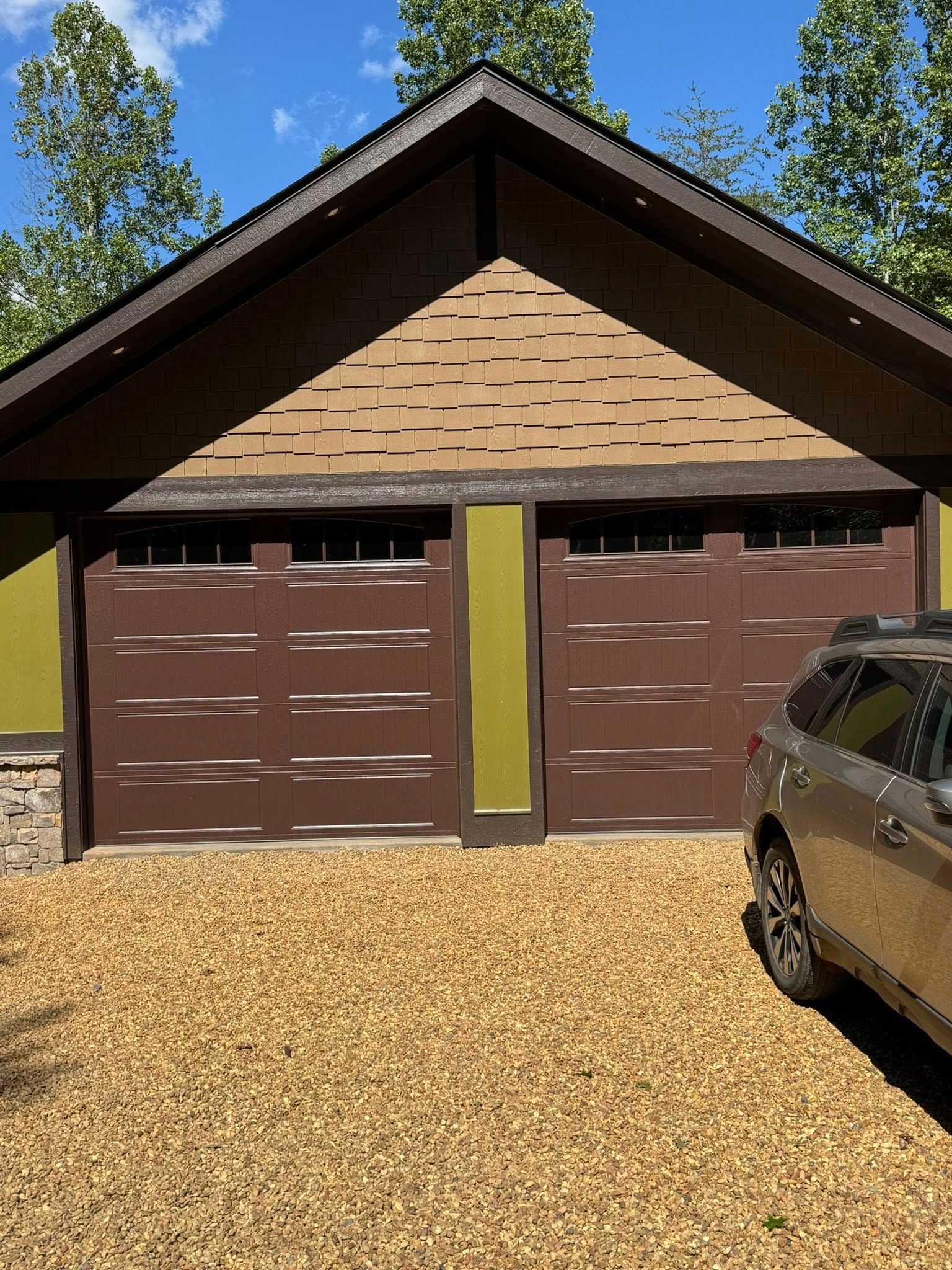 Two-car garage with brown doors, tan siding, and gravel driveway under a blue sky