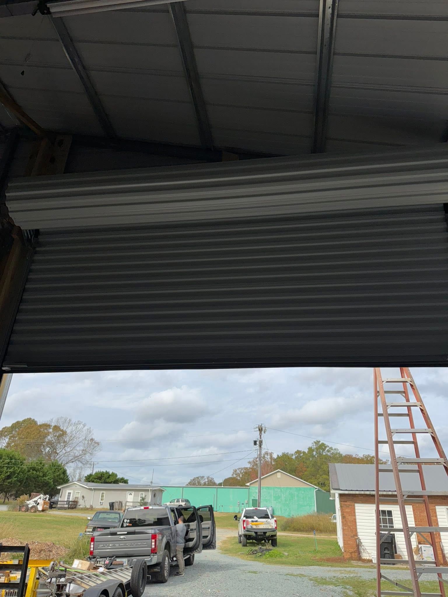 Open garage door framing a yard with two trucks, a ladder, and a partly built shed.