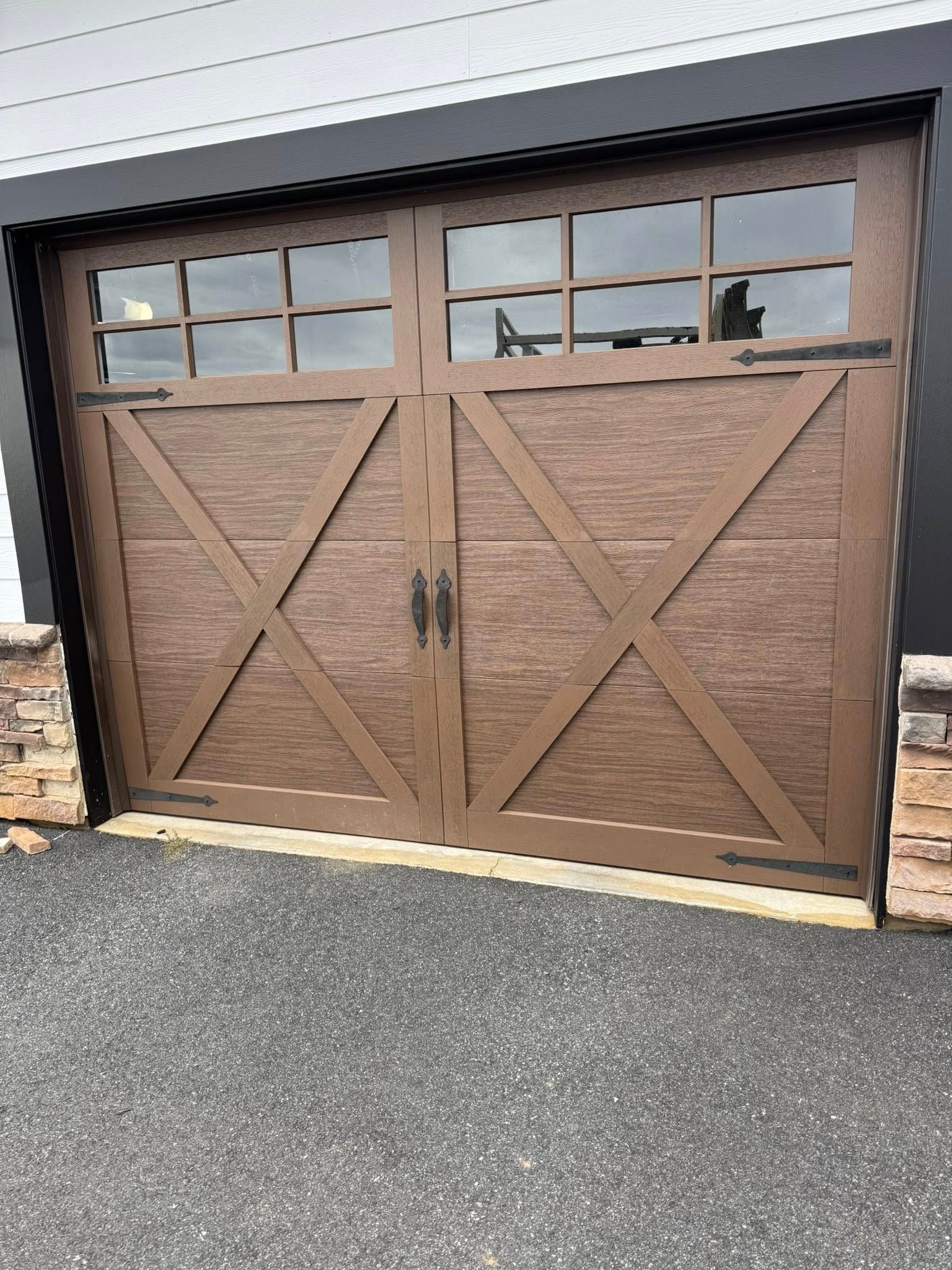 Brown wooden garage door with X-brace panels and windows at top, set in a black metal frame.