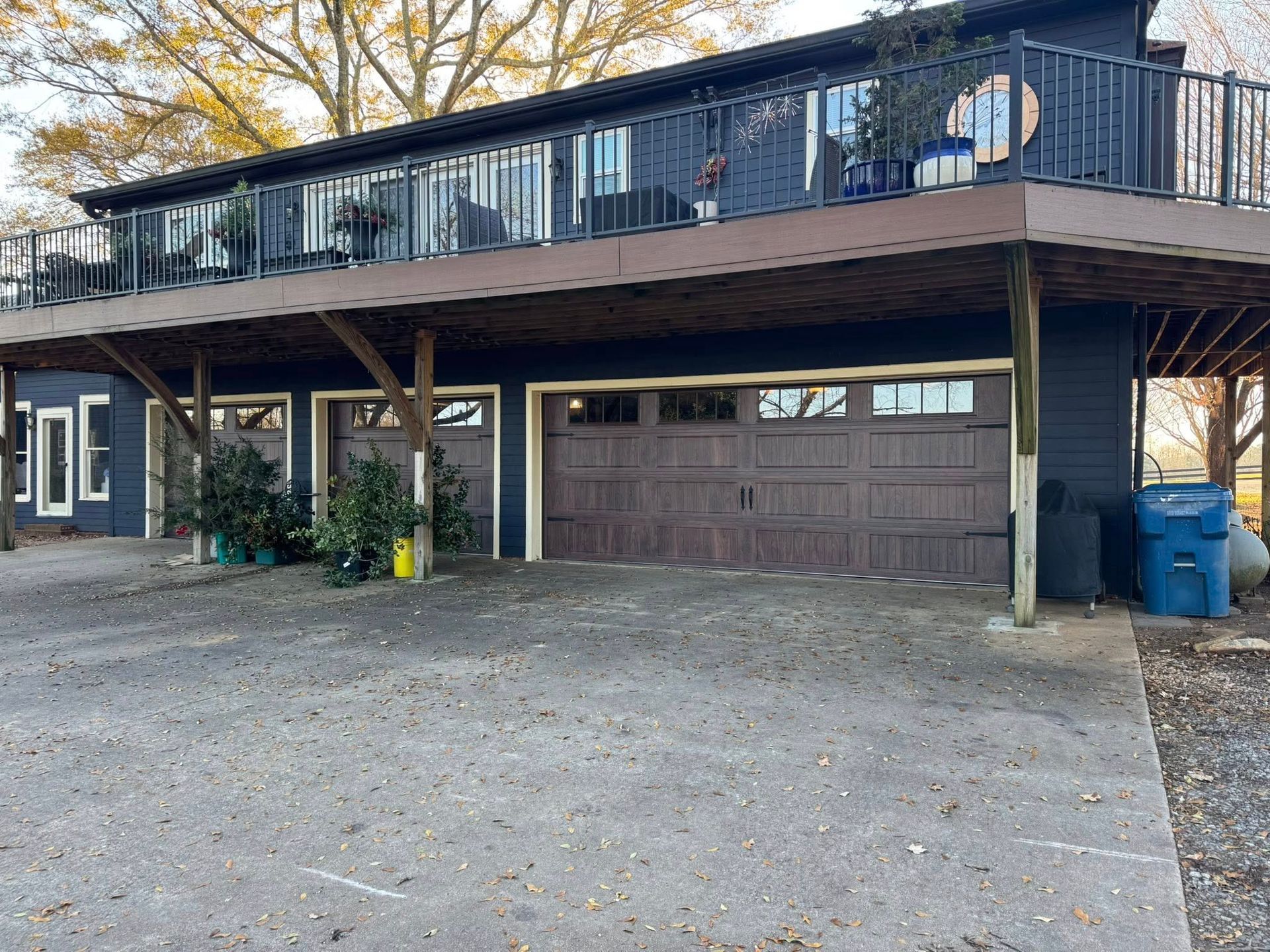 Two-story house with a raised wooden deck, garage below, and gravel driveway in front.