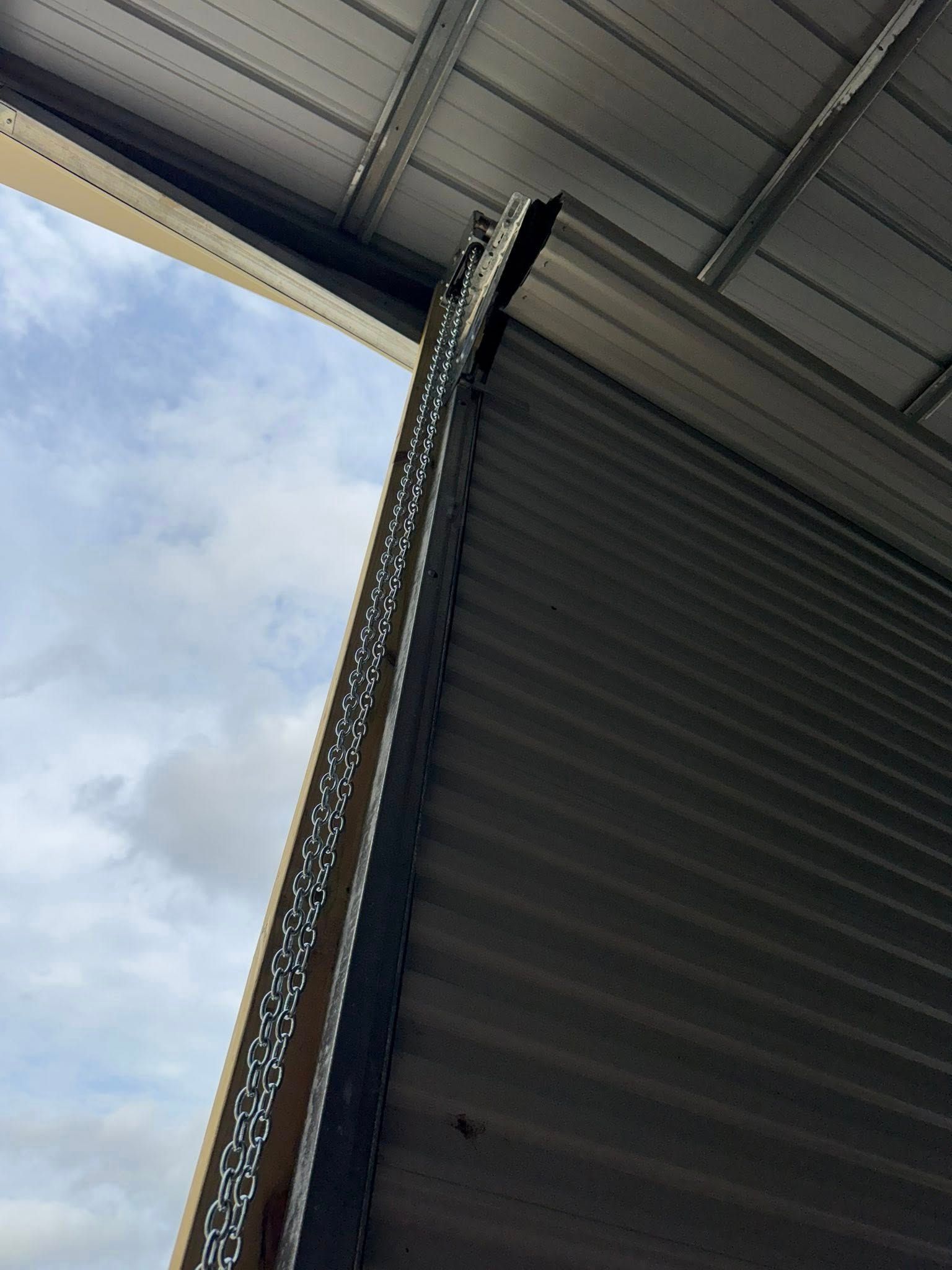 Tall speaker column hanging under a metal roof against a cloudy sky.